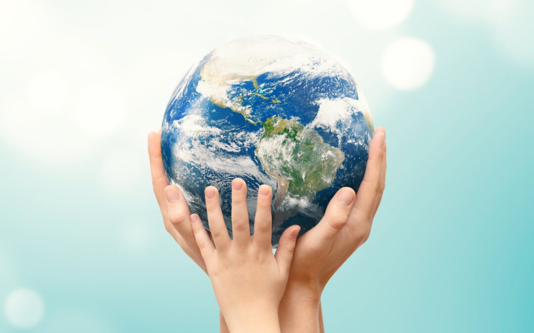 Two sets of hands cradling a globe against a soft blue background representing Earth Day and environmental awareness