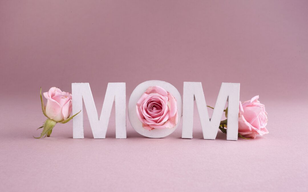 White letters spelling MOM surrounded by pink roses on a soft pink background for Mother's Day in Bryan Texas