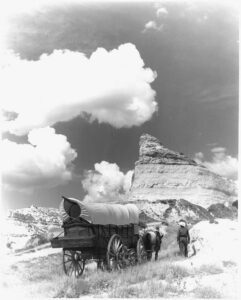 Black and white photo of a Conestoga covered wagon and horse on the Oregon Trail with rocky buttes in the background