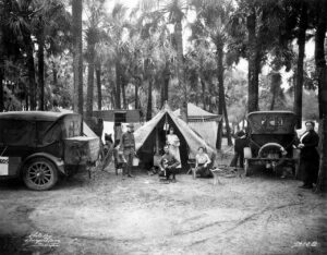 Black and white photo of early car campers with two Model T automobiles and a canvas tent set up between palm trees in Tampa Florida circa 1920s