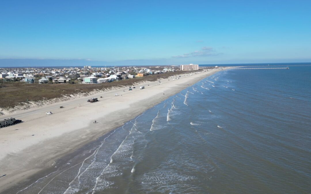 Aerial view of RVs and trucks parked on the beach at Port Aransas, Texas, with beach houses along the dunes.